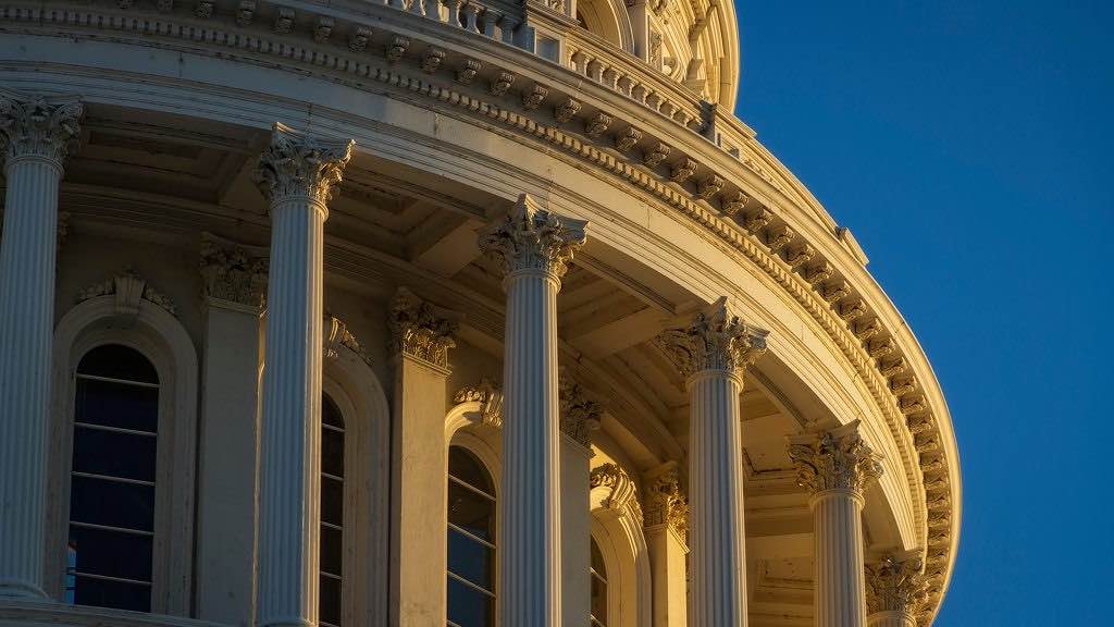 Close-up of a curved neoclassical portico with tall fluted columns and ornate capitals against a blue sky