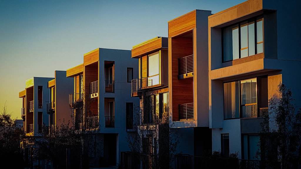 Contemporary apartment complex bathed in warm sunset light, with balconies and large windows facing the sun.